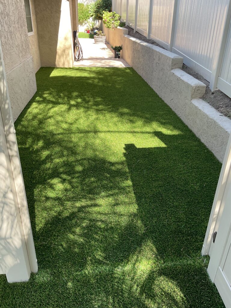 Synthetic turf has been installed in a narrow side yard between the stucco house and a block retaining wall. The...
