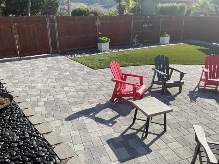 Finished backyard showing a large interlocking paver patio adjacent to a rectangular artificial turf lawn with a...