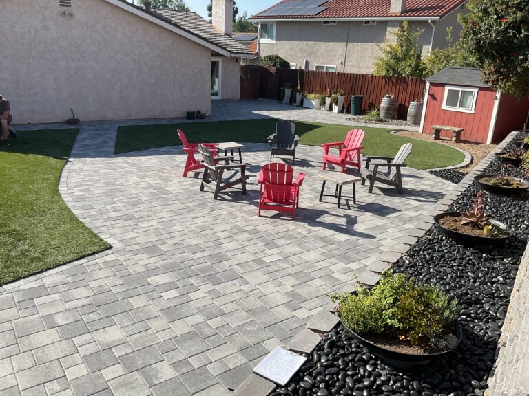 Finished backyard showing interlocking paver patio with adjacent artificial turf inserts and a low segmental retaining...