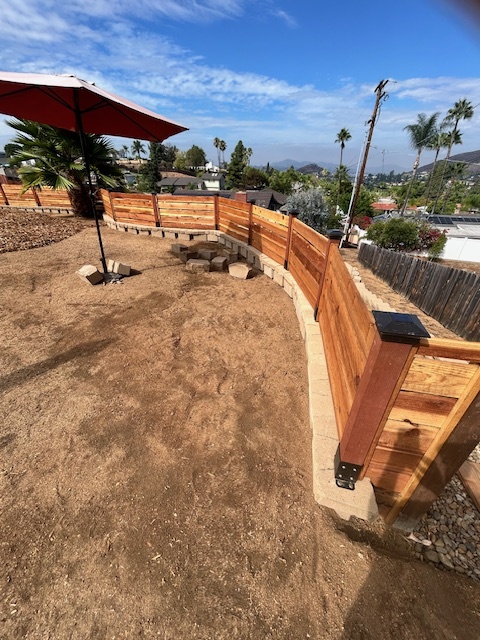 Backyard shows a newly constructed segmental retaining wall with attached cedar wood fence panels mounted to concrete piers using metal post brackets. El Cajon project by Install It Direct.