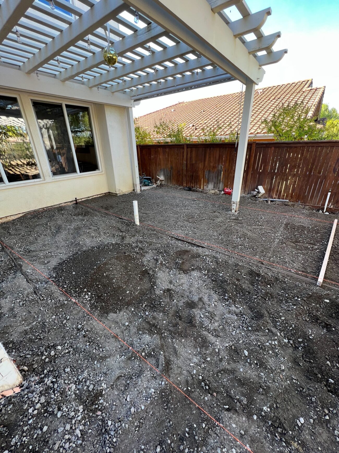 Backyard patio area under a pergola with crushed rock/subbase compacted and string lines laid out to mark the paving...