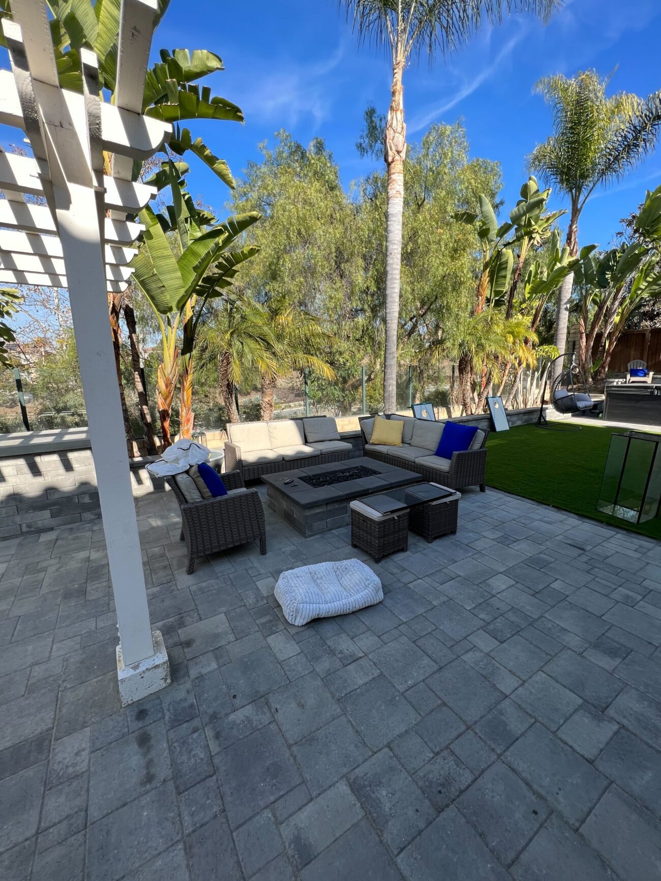 Finished interlocking paver patio with integrated fire pit and outdoor seating adjacent to a newly installed artificial...