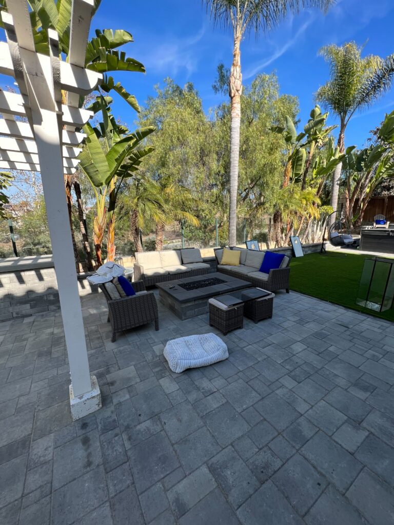 Finished interlocking paver patio with integrated fire pit and outdoor seating adjacent to a newly installed artificial...