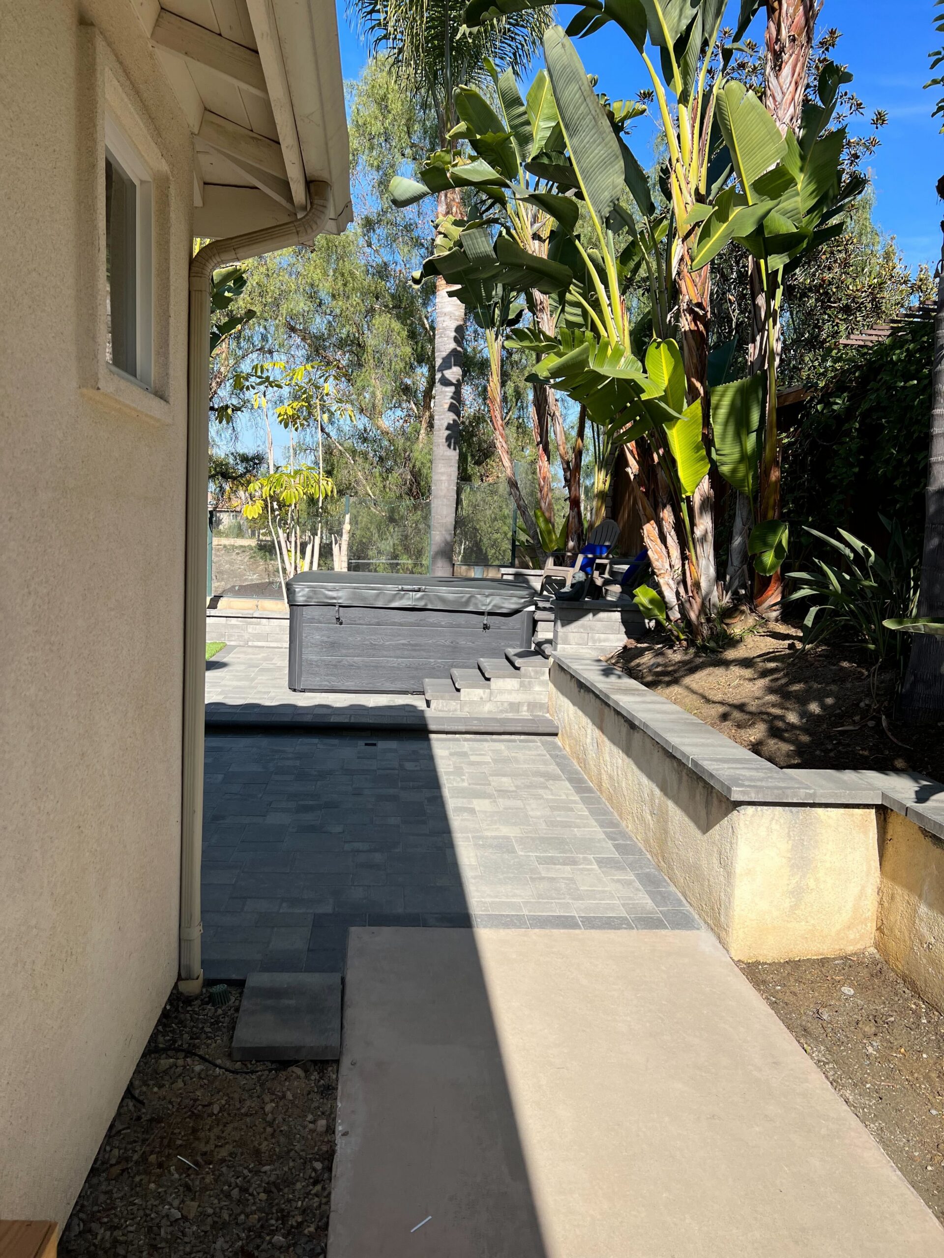 Finished side-yard paver walkway with capped planter wall and spa access in Carlsbad.