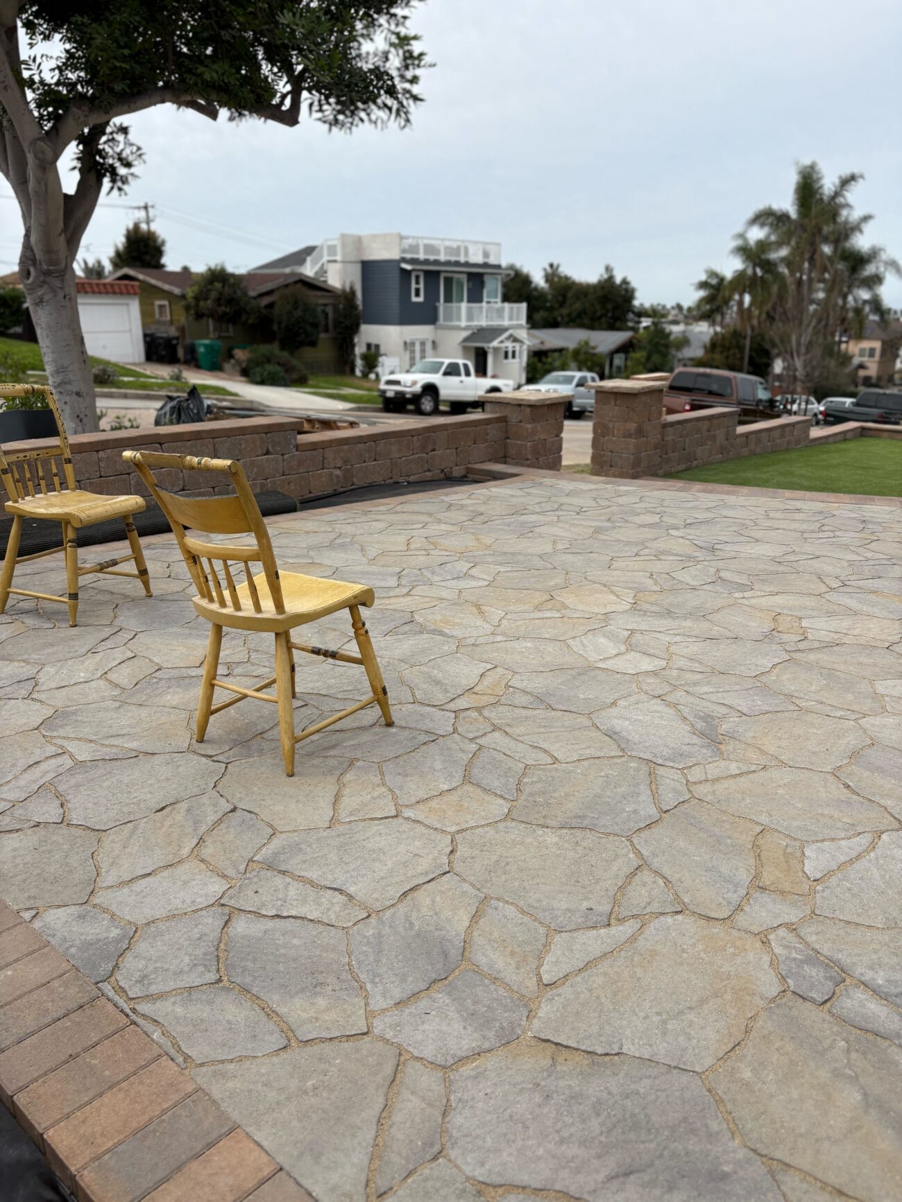 Finished flagstone-pattern paver terrace with a brick soldier-course border, the capped seat wall along the street.