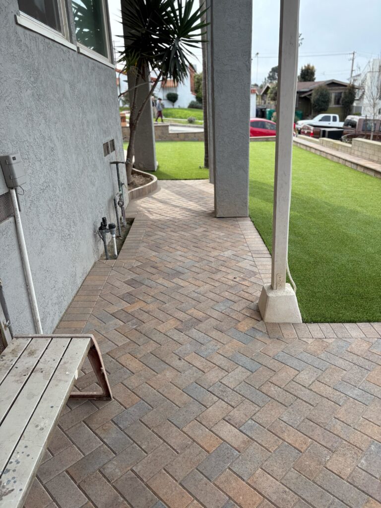 Finished residential paver patio and walkway installed in a herringbone pattern adjacent to newly installed artificial...