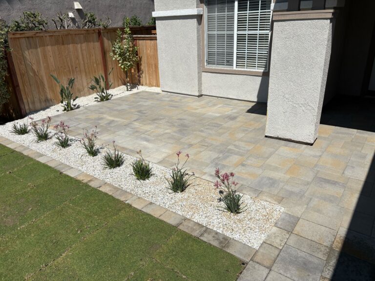 Finished interlocking paver patio adjacent to a stucco house with a paver border and a narrow decorative gravel planting strip containing drought-tolerant plants. San Marcos project by Install It Direct.