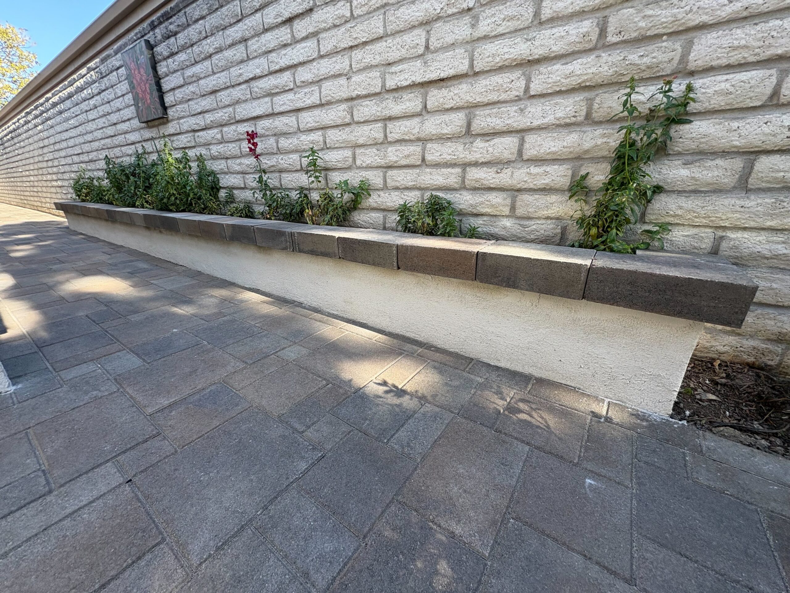 A stucco-finished planter wall capped with a paver coping course runs the length of the new walkway.