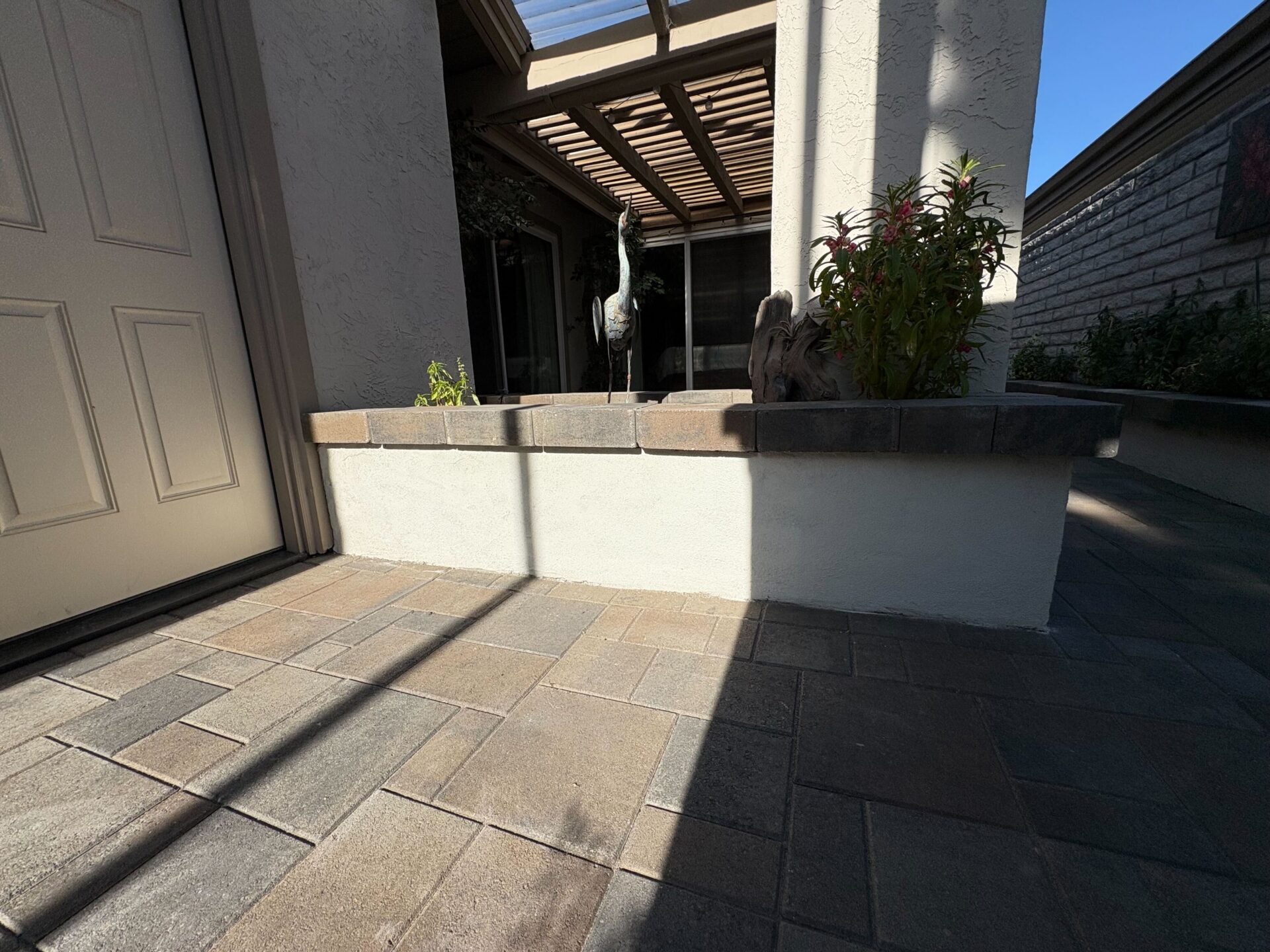 Finished residential entry/patio showing interlocking pavers laid in a rectangular pattern adjacent to a capped raised...