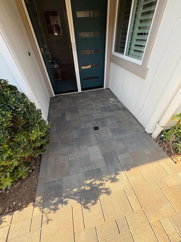 Front entry landing and adjacent walkway paved with interlocking concrete pavers in a modular pattern. A central recessed...