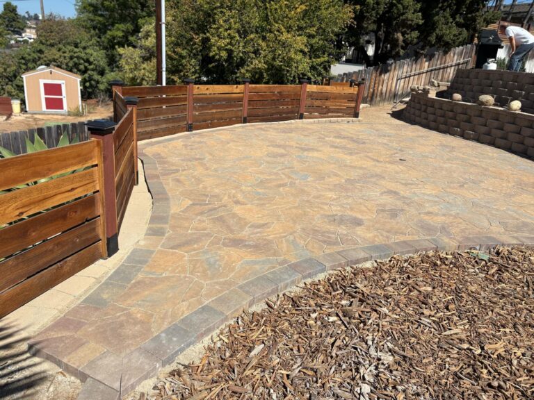 Completed curved patio using flagstone-style interlocking pavers with a contrasting soldier course border. A segmental...