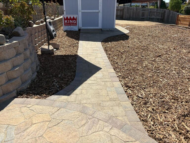 Interlocking paver walkway with a curved band and circular soldier-course transition leads to a small shed at the rear of...