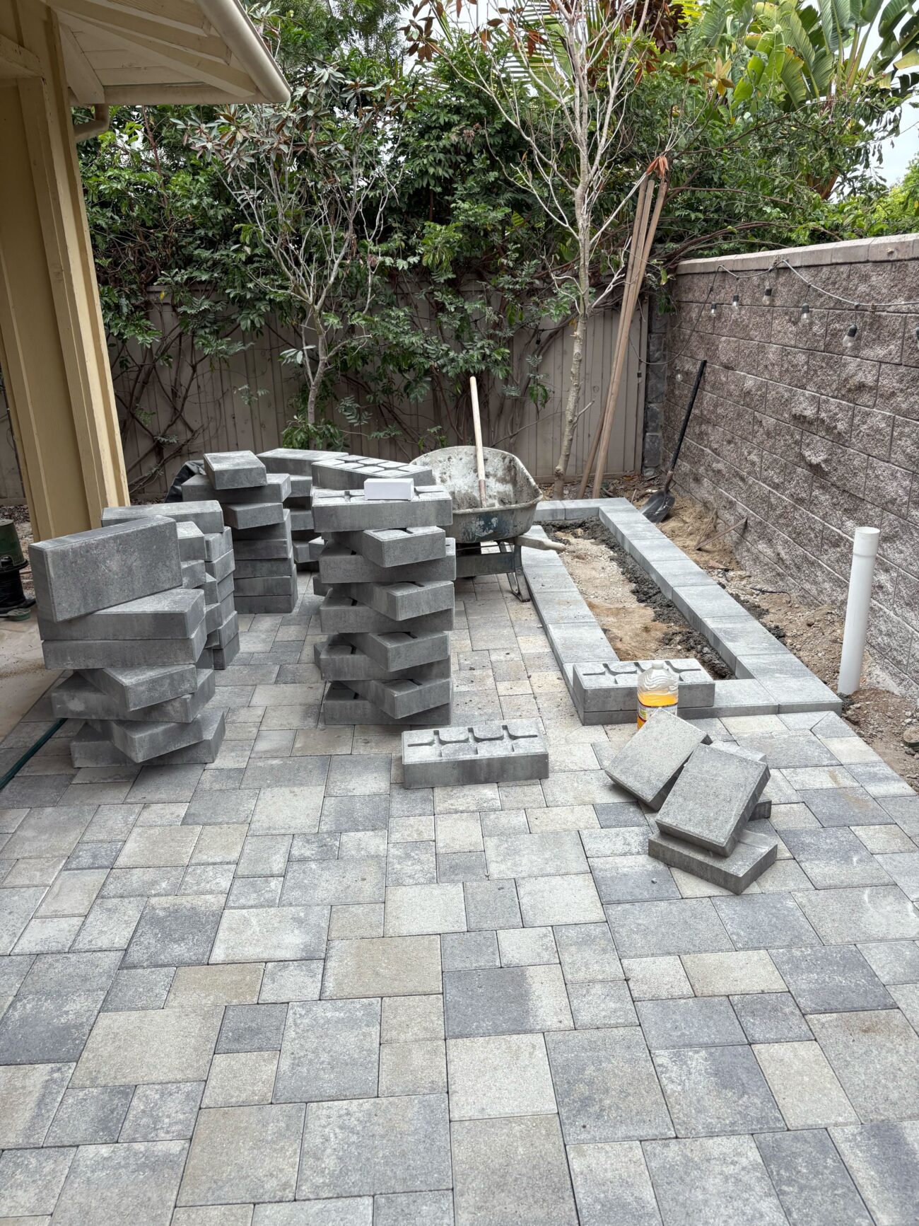 Backyard paver patio installation in progress showing a large field of interlocking pavers installed, stacks of...
