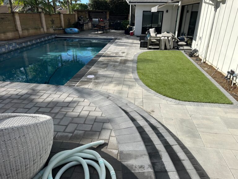 Residential backyard showing a completed paver pool deck with a curved set of paver steps and an adjacent artificial turf insert. San Diego project by Install It Direct.