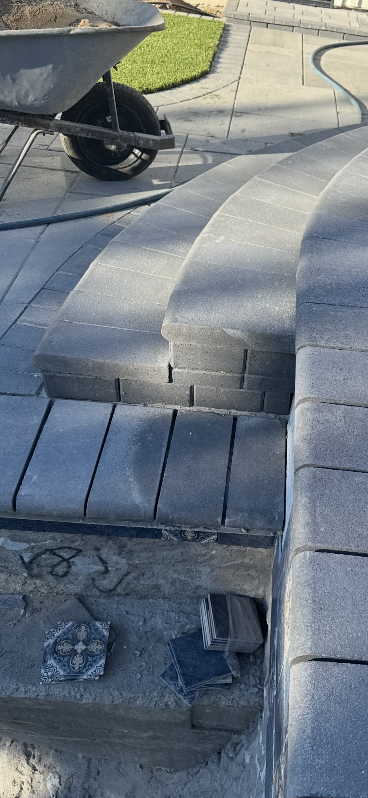 Close-up of curved interlocking paver steps and segmental wall coping during installation. San Diego project by Install It Direct.