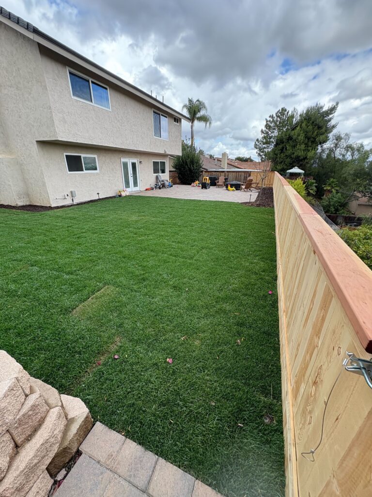 Backyard shows a finished artificial turf lawn adjoining a new paver patio and a recently installed wooden privacy fence. El Cajon project by Install It Direct.