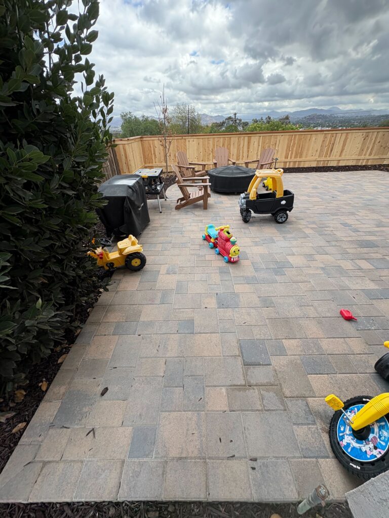 Finished interlocking paver patio in a backyard setting with a new wooden fence, outdoor seating and a round fire pit. El Cajon project by Install It Direct.