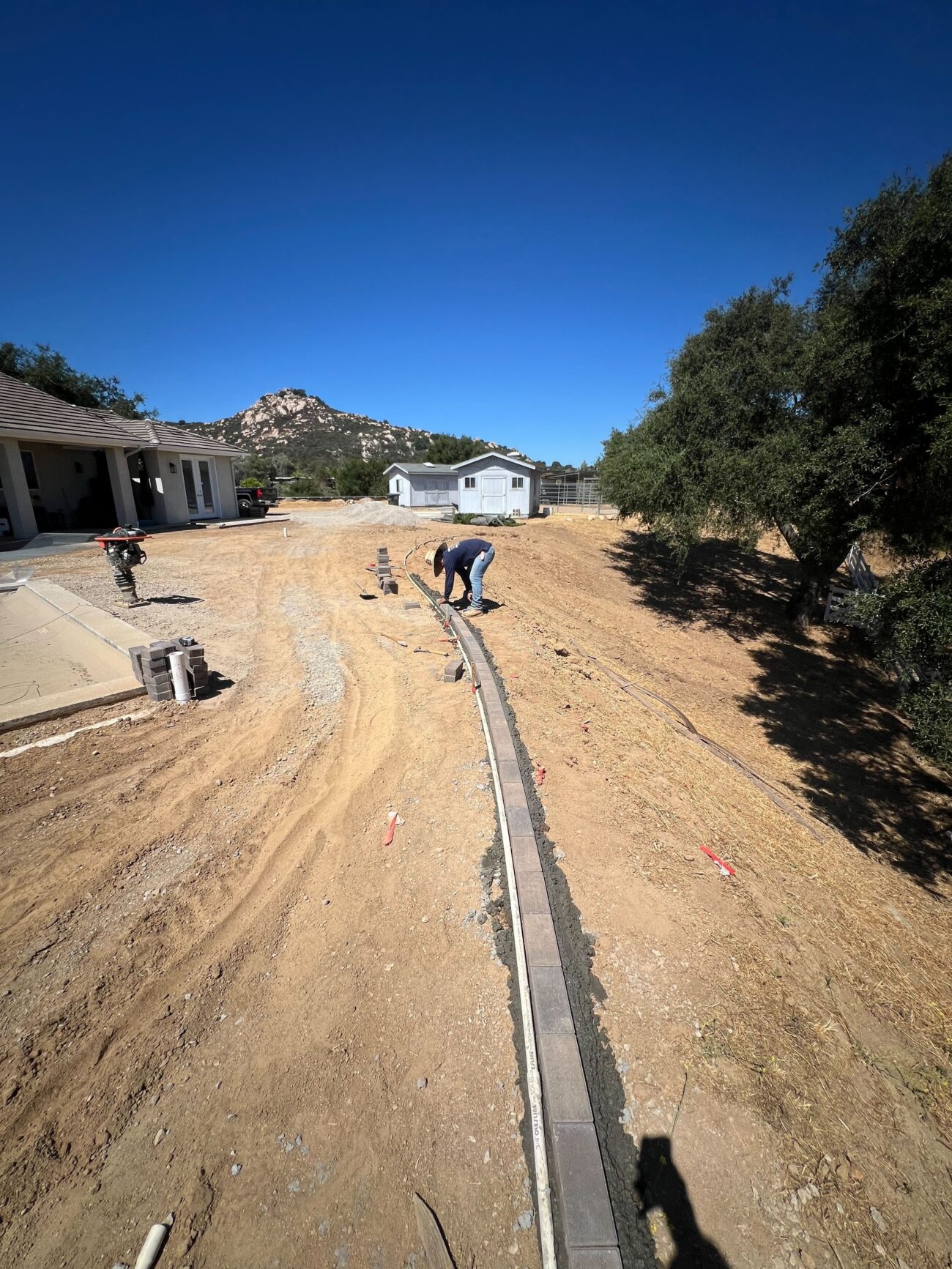 Residential backyard site with a crew member installing a curved segmental concrete block curb / low retaining wall on a...