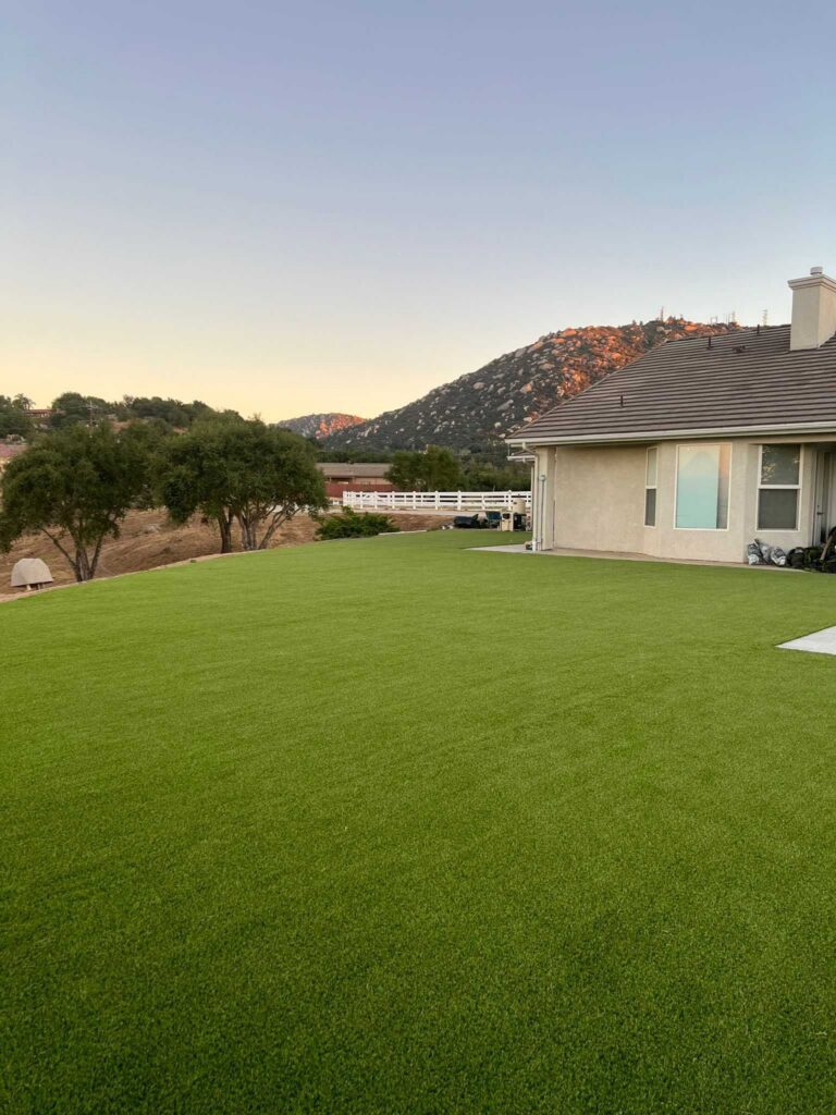 Finished residential backyard with newly installed artificial turf adjacent to the home's exterior. Clean, uniform...