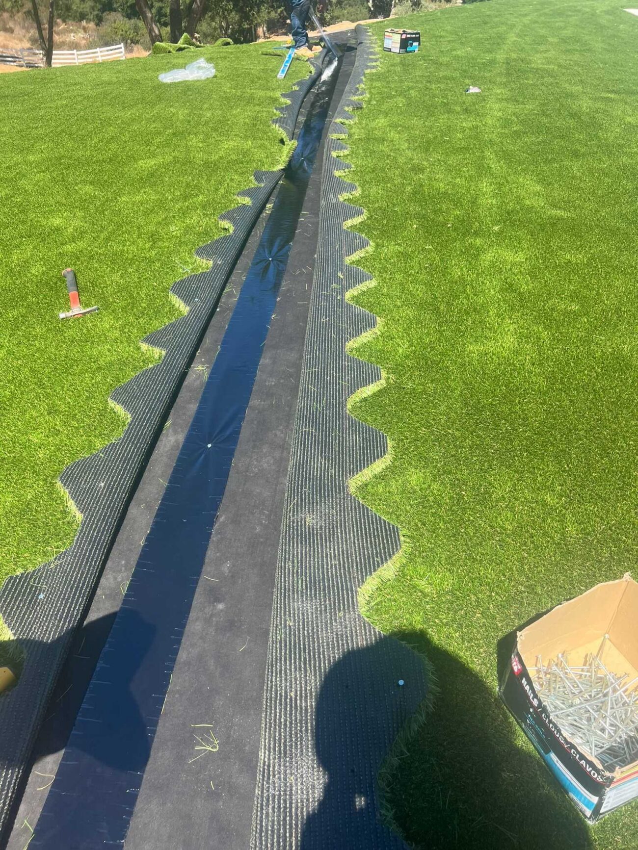 Artificial turf installation in progress showing a long seam with seam tape/underlayment exposed and turf edges trimmed...