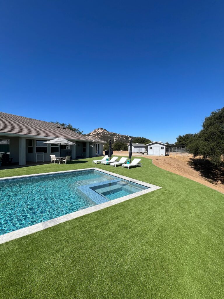 Residential backyard showing a completed pool and attached spa edged with concrete coping and surrounding artificial...