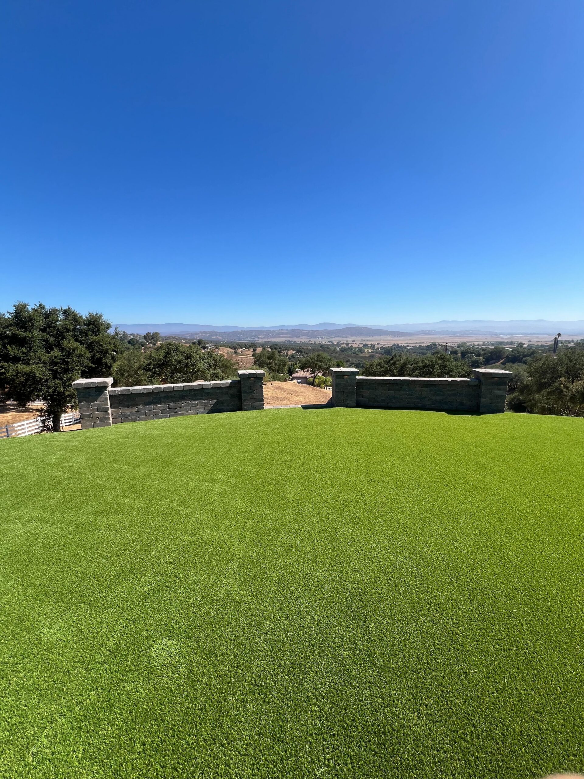 Artificial turf and Angelus Rustic Wall Stone segmental retaining walls with capped pillars, valley view beyond.
