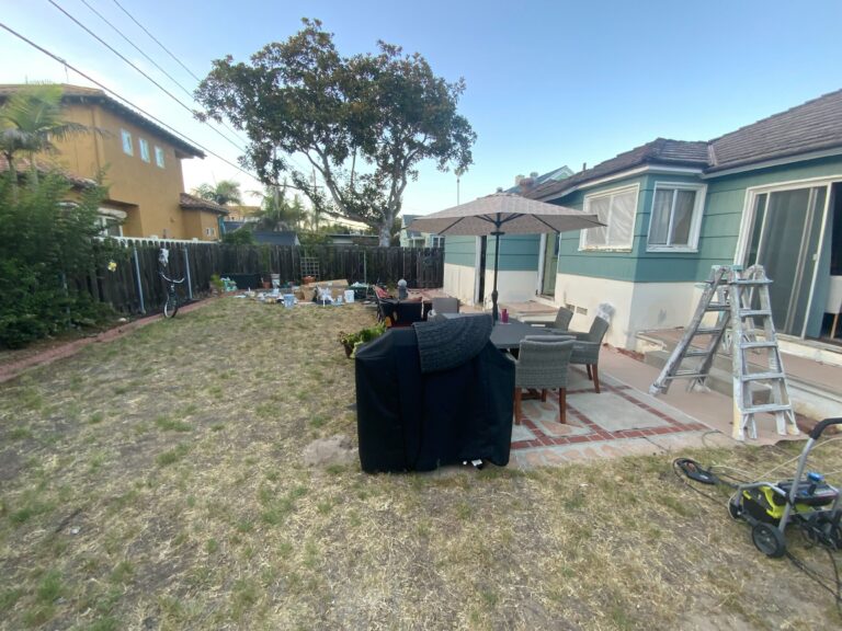 Backyard site shows an existing small paver patio with outdoor furniture and an umbrella adjacent to a patchy natural...