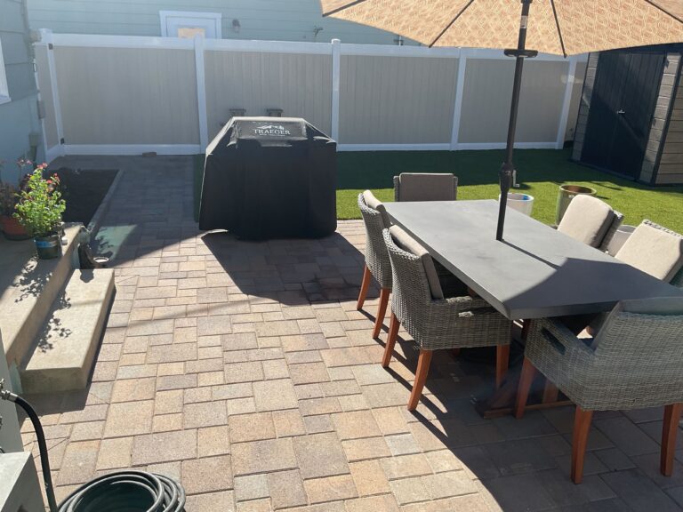 Finished backyard patio featuring interlocking pavers laid in a running/bond pattern with a dining table, umbrella, and...