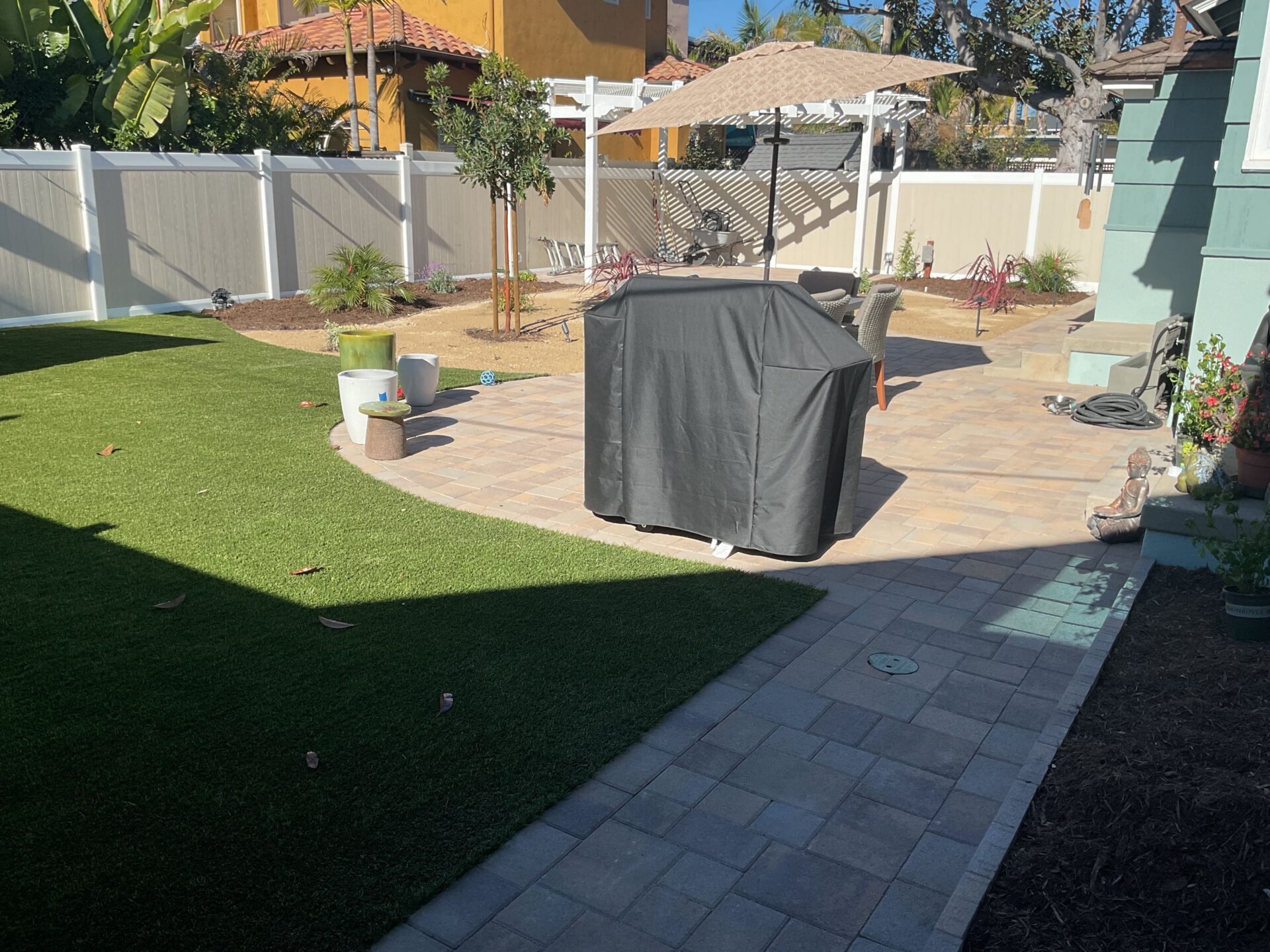 Finished residential backyard showing a newly installed paver patio and matching paver walkway with artificial turf lawn...