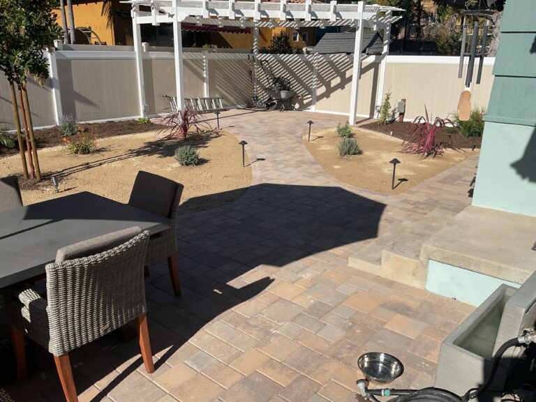Finished interlocking paver patio and connecting walkway with a pergola and planted beds; low-profile path lights and...