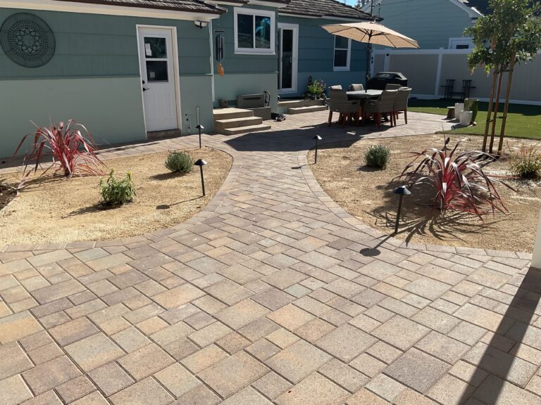 Residential backyard with a recently installed interlocking paver patio and curved walkway laid in a modular/ashlar...