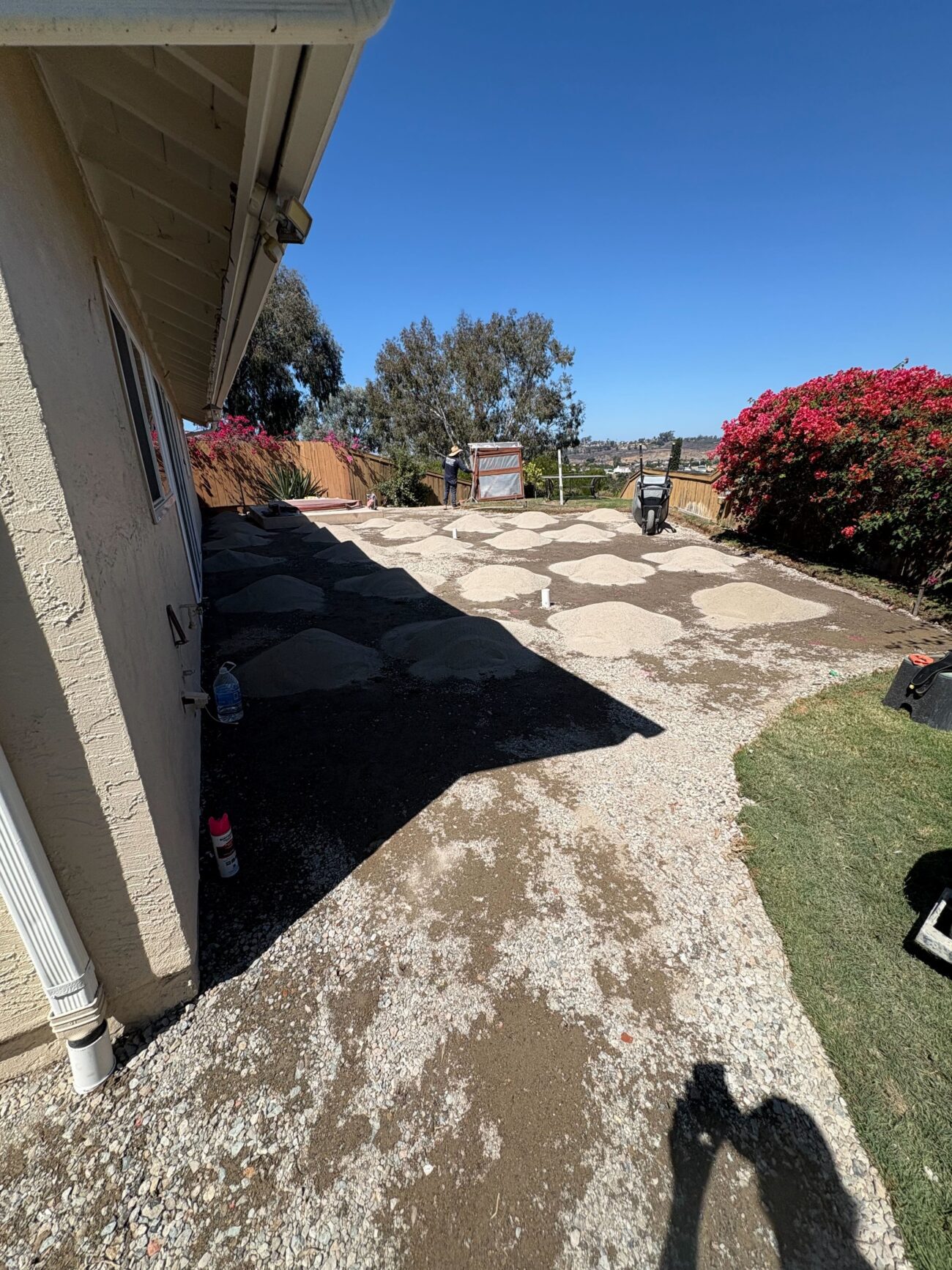 Backyard patio area with existing pavers removed, exposing the aggregate subbase and patchy bedding sand across the...