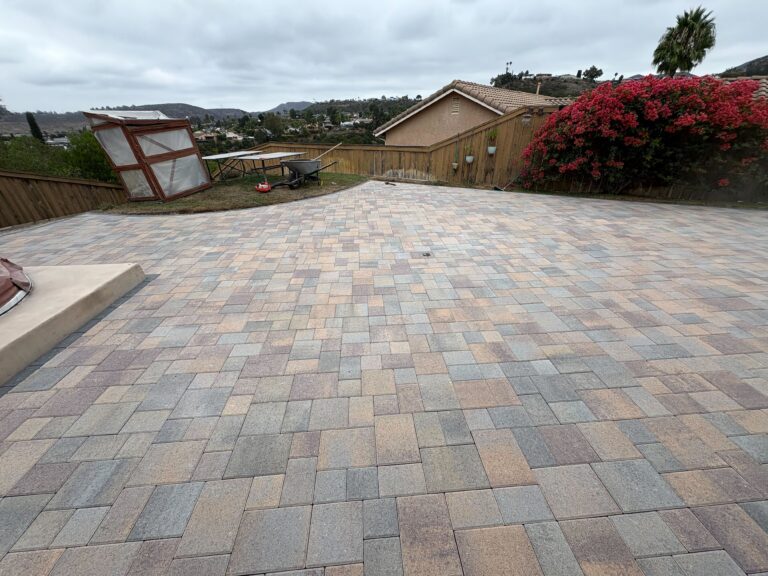 Finished interlocking paver patio in a residential backyard showing multi-color concrete pavers installed in an...