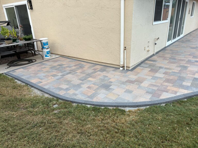 Finished residential paver patio with interlocking pavers laid in a multi-color pattern and a darker soldier-course...