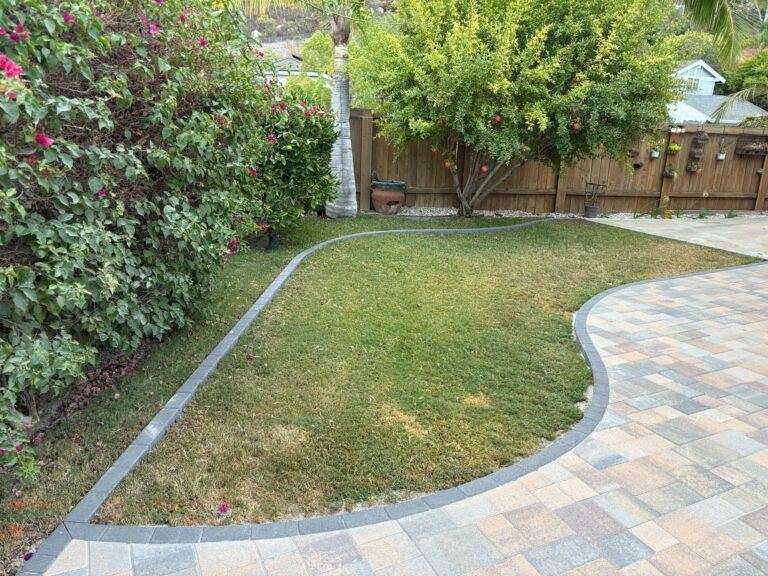 Curved interlocking paver patio and walkway with a matching edge restraint bordering a small patch of natural grass....