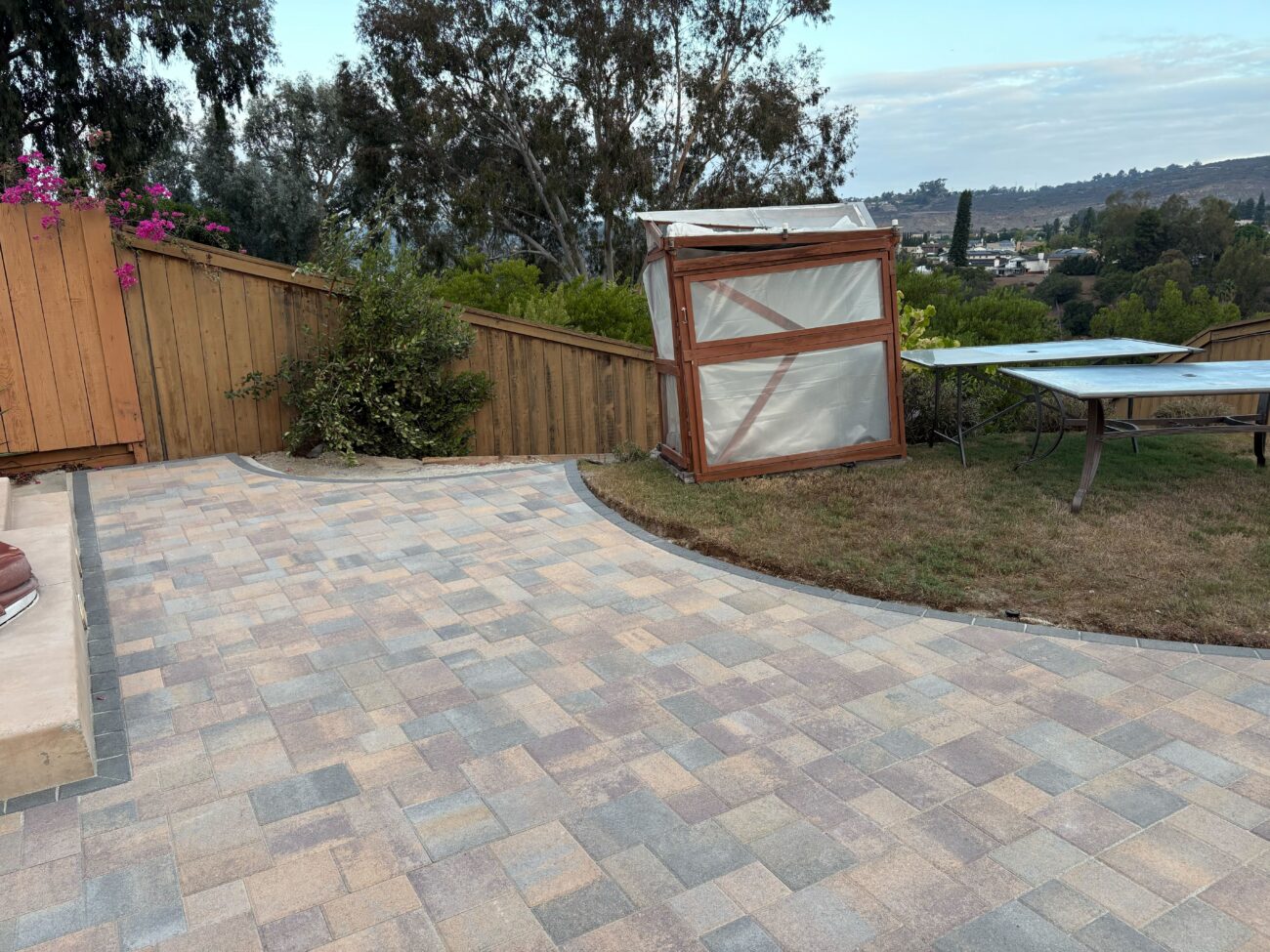 Residential backyard showing a newly installed interlocking paver patio with a smooth curved edge abutting existing...