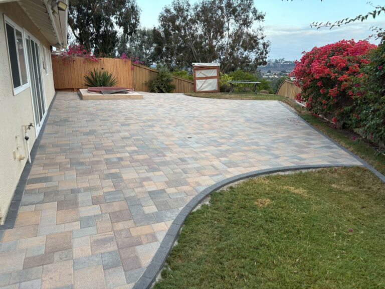 Completed interlocking paver patio adjacent to a residential exterior with a curved edge meeting existing natural grass....