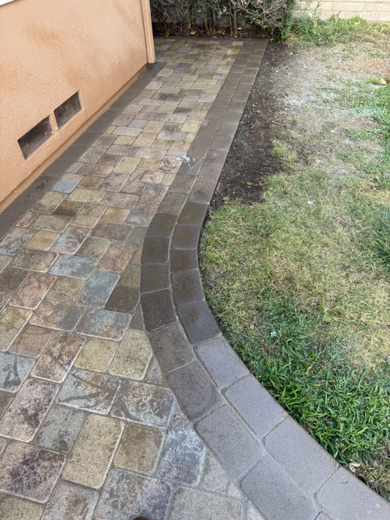 Curved interlocking paver walkway/patio installed along the side of a house, showing a soldier-course style border and a...