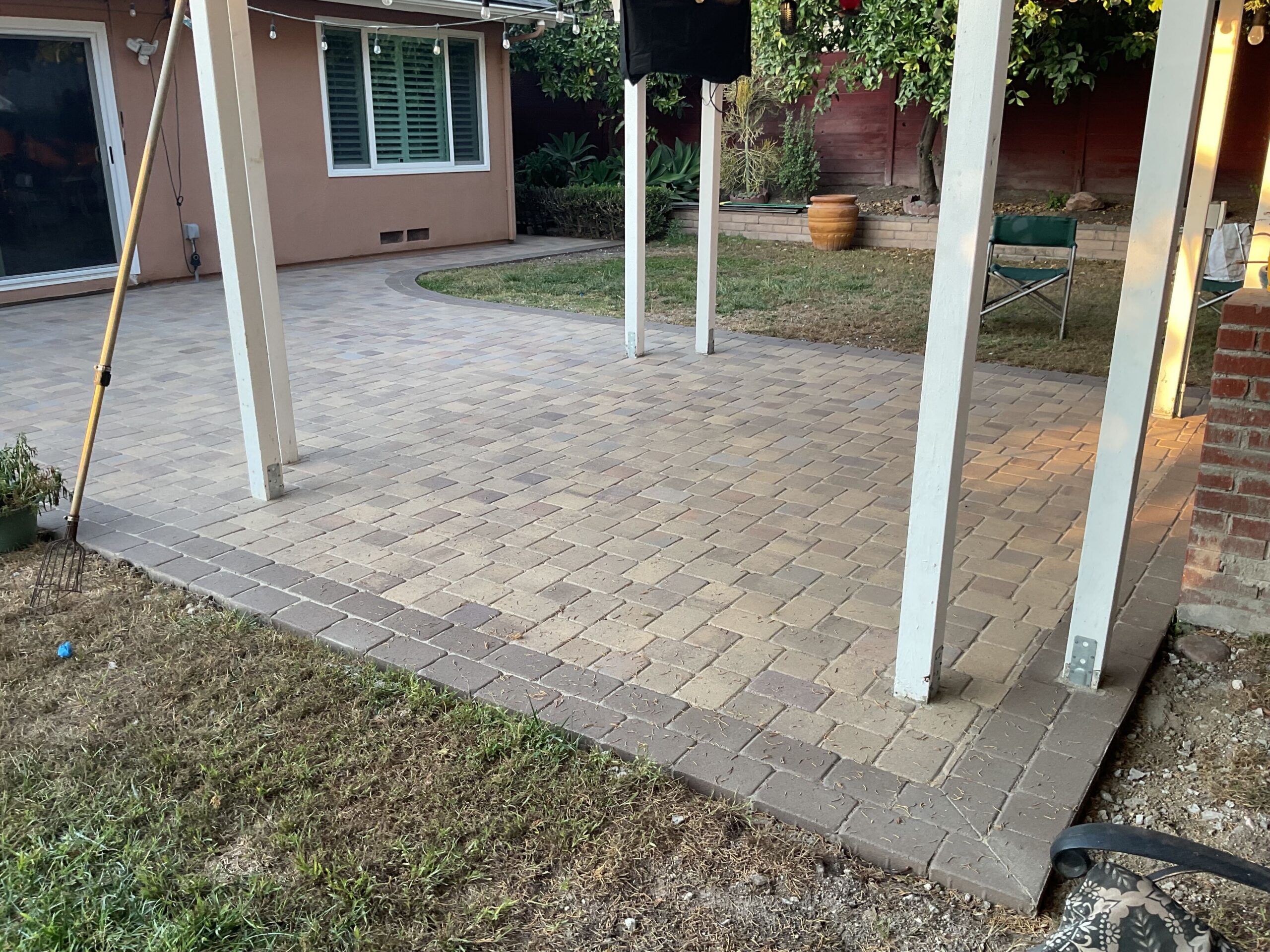 Interlocking paver patio with a soldier-course border beneath a patio cover; vertical support posts are anchored through...