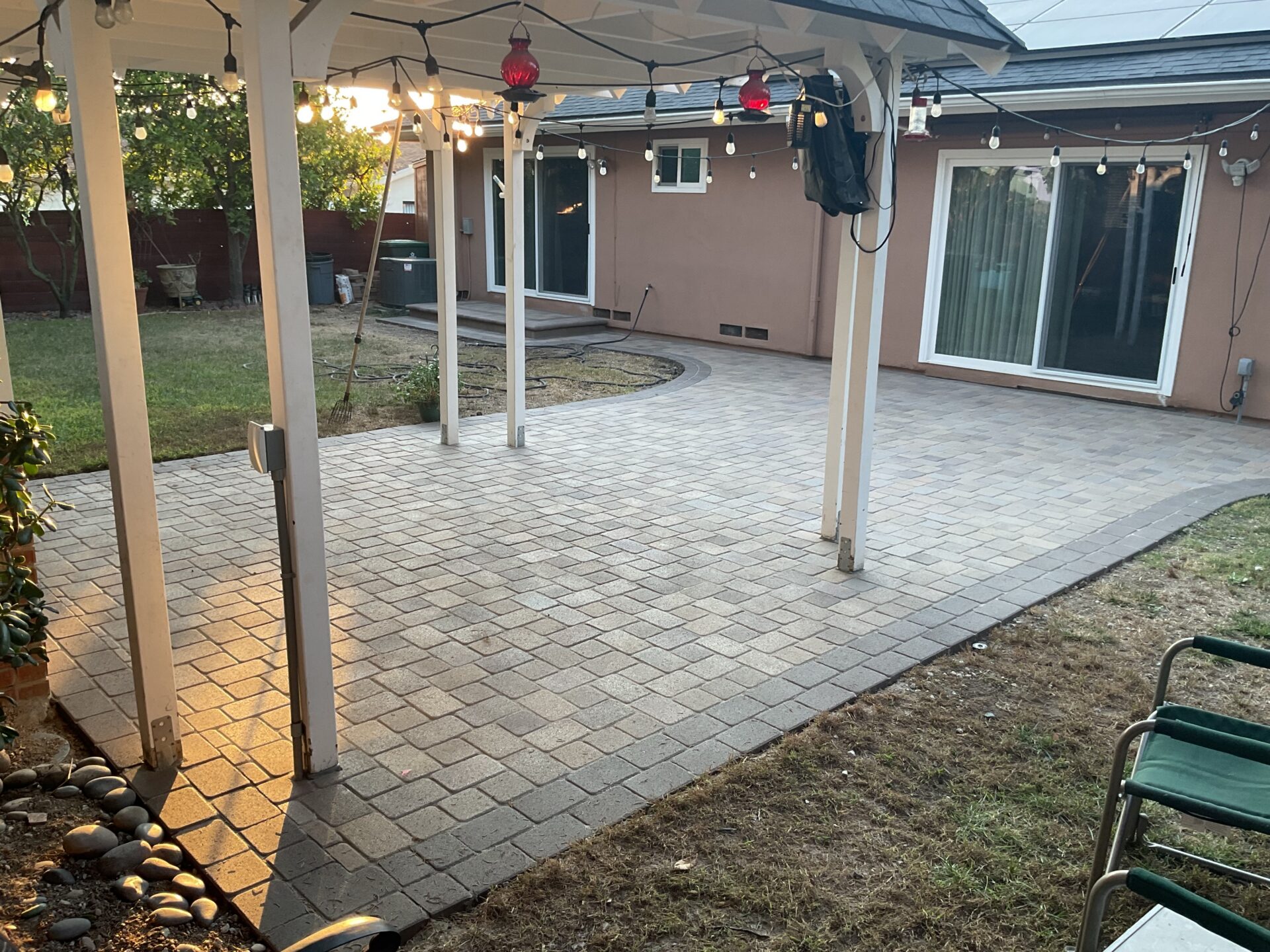 Finished interlocking concrete paver patio with a curved edge and defined border installed under a patio cover. White...