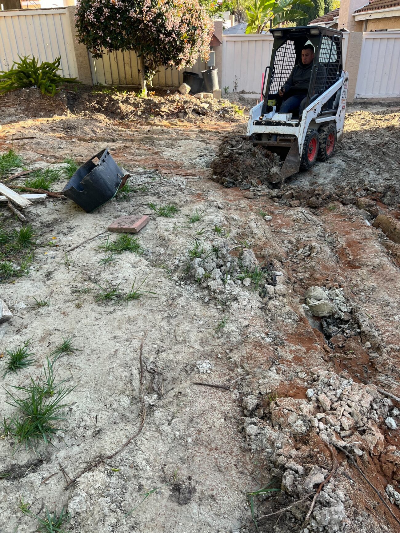 Bobcat skid-steer mid-grade in cleared backyard. Strongest single demolition frame — heavy equipment in action, fully...