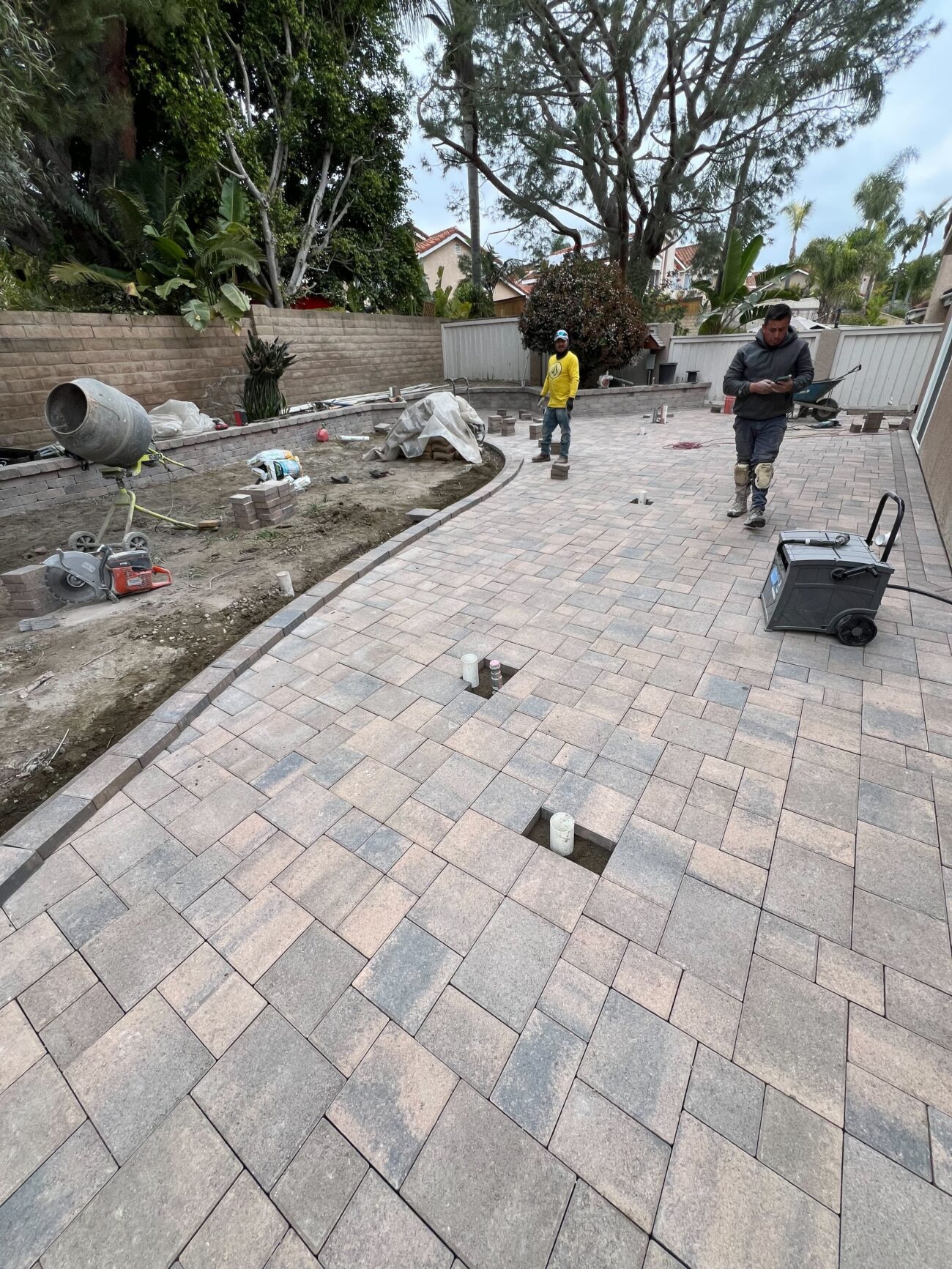 Two crew members on a partly-laid backyard patio with a cement mixer. Different vantage and phase moment than the...