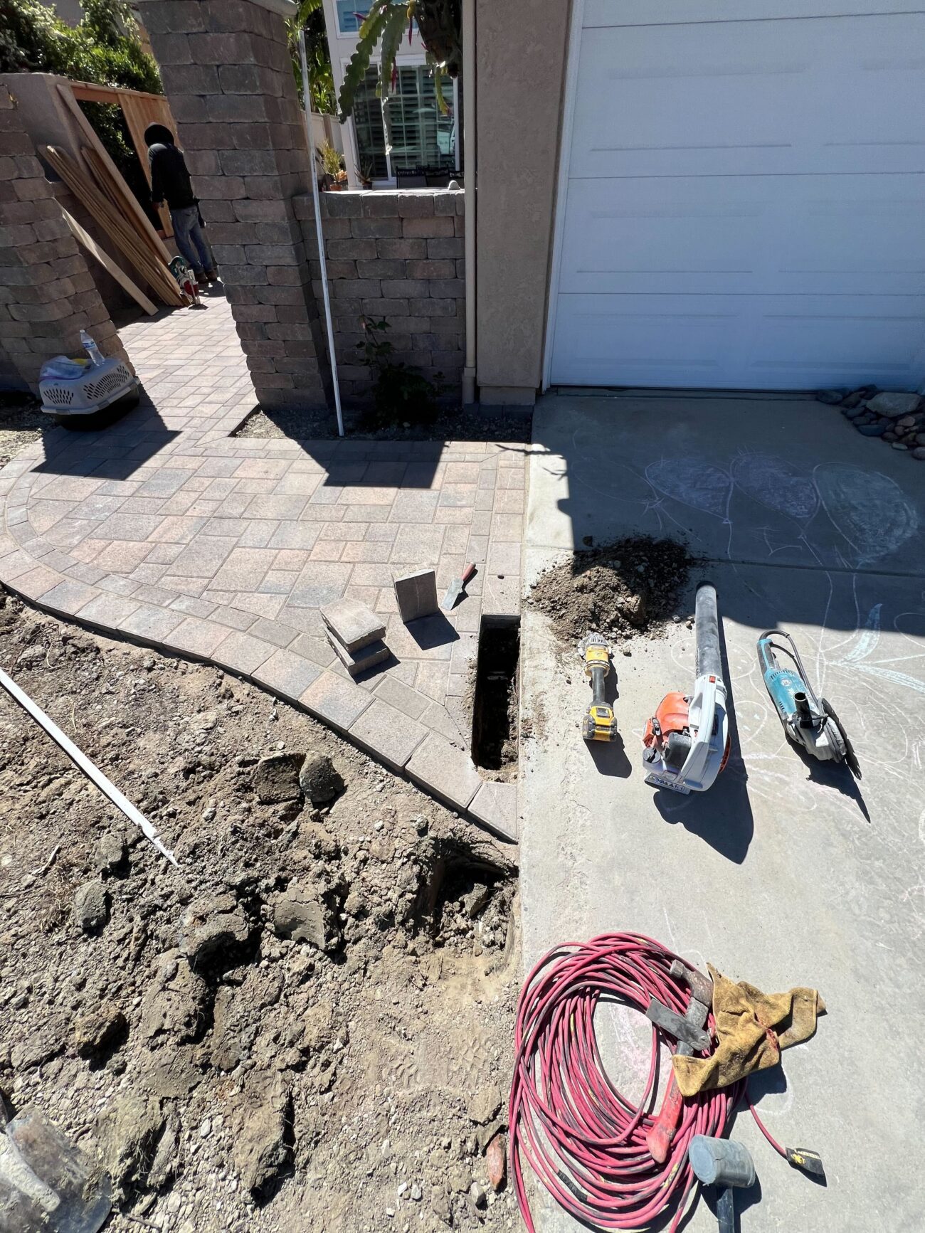 Overhead-angle frame of half-laid paver pattern at the front courtyard near the new pillars. Strongest single...