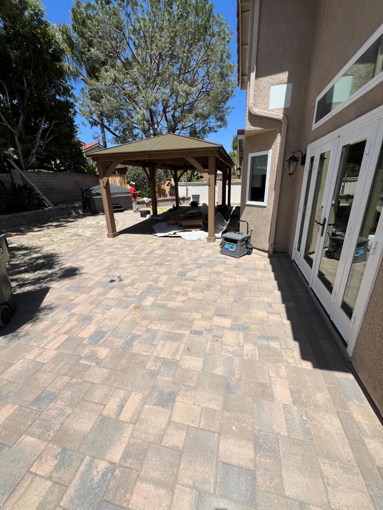 Pergola / gazebo framing erected over the finished backyard pavers — captures the finishing/feature-install phase that...