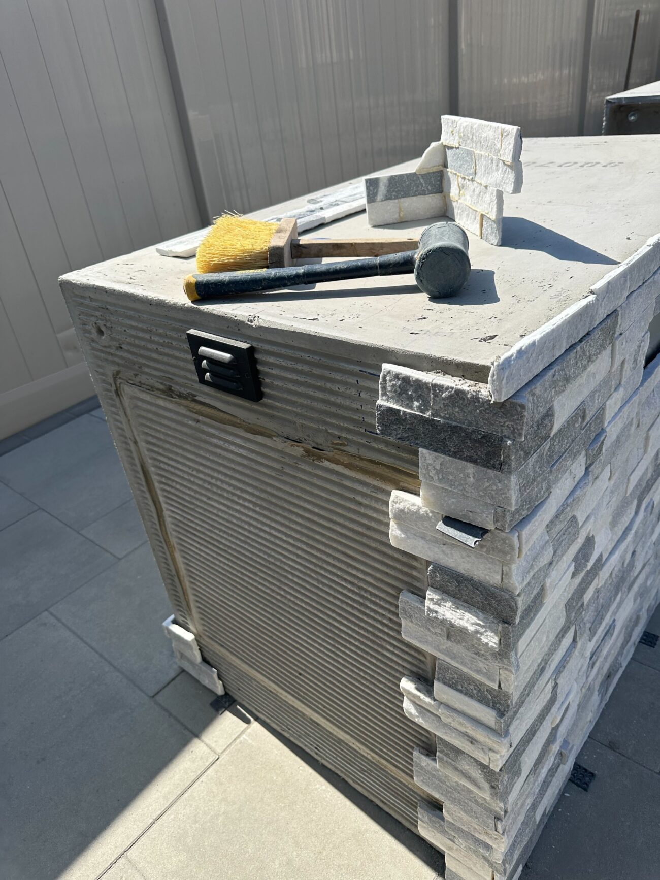 Stone veneer installation in progress on an outdoor kitchen/pillar unit. Corner returns and stacked ledgestone pieces are...