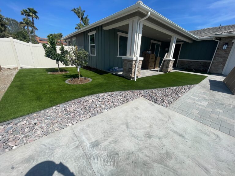 Finished residential front yard showing installed artificial turf with two newly planted trees, a paver patio and paver...