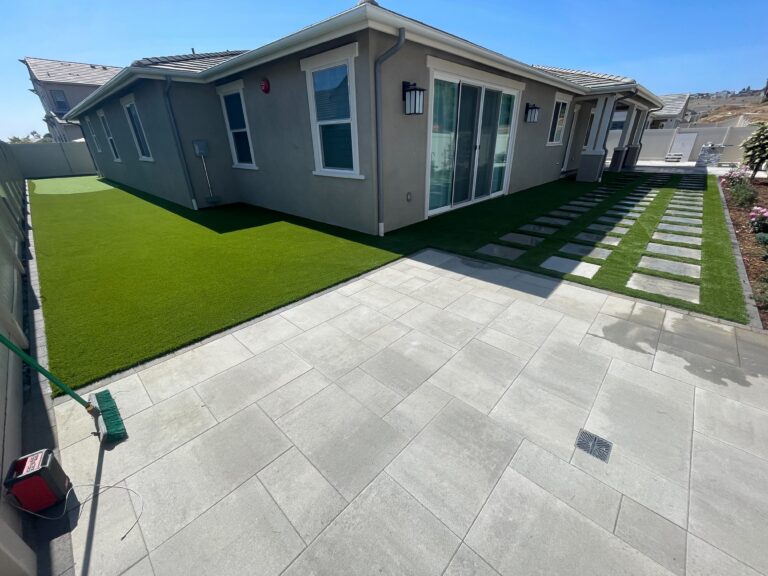 Finished backyard hardscape showing a large-format paver patio transitioning to a stepping-stone paver walkway set in...