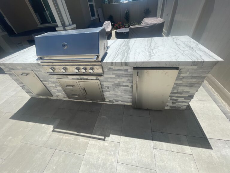 Completed outdoor kitchen island with a built-in stainless gas grill, refrigerator and storage drawers set into a stone...