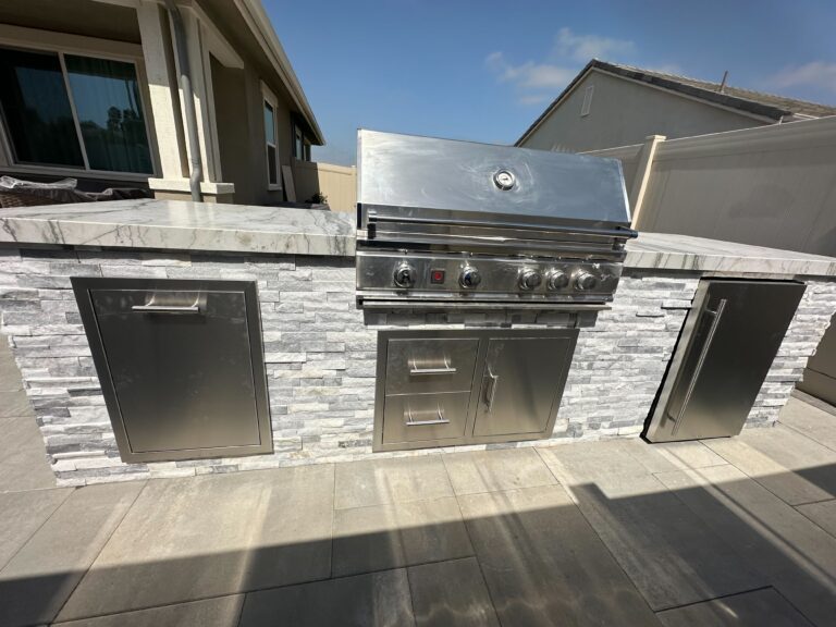 Residential outdoor kitchen built into a stone veneer island featuring a built-in stainless steel gas grill, multiple...