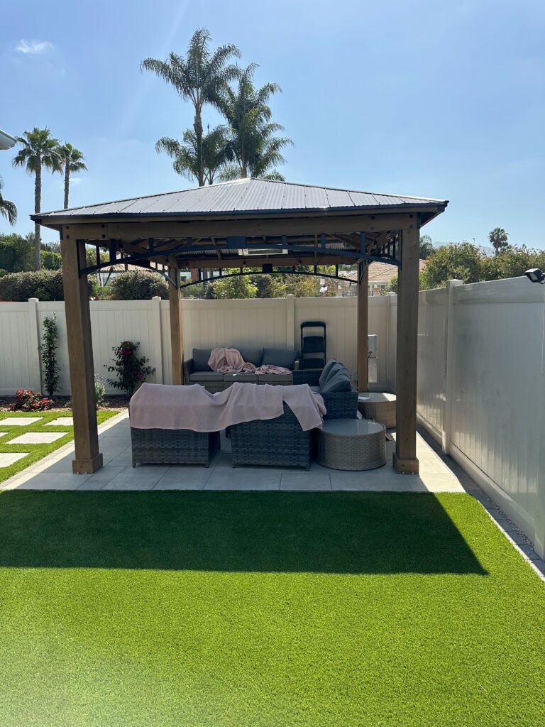 Completed backyard outdoor living area featuring installed artificial turf and a freestanding pergola/covered seating...